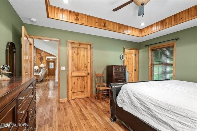 bedroom with light wood-type flooring, ceiling fan, and a tray ceiling