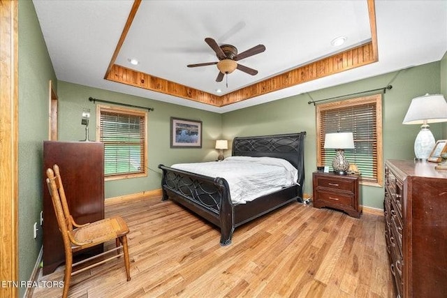 bedroom featuring light wood finished floors, ceiling fan, a tray ceiling, and baseboards