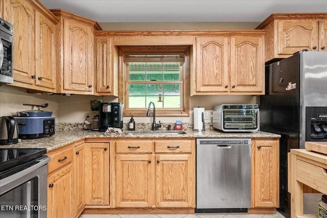 kitchen featuring light stone counters, a toaster, stainless steel appliances, light brown cabinets, and a sink