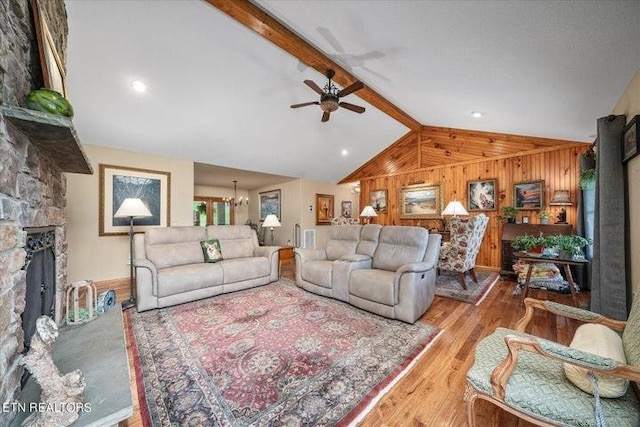 living area featuring wooden walls, vaulted ceiling with beams, light wood-type flooring, a fireplace, and ceiling fan with notable chandelier