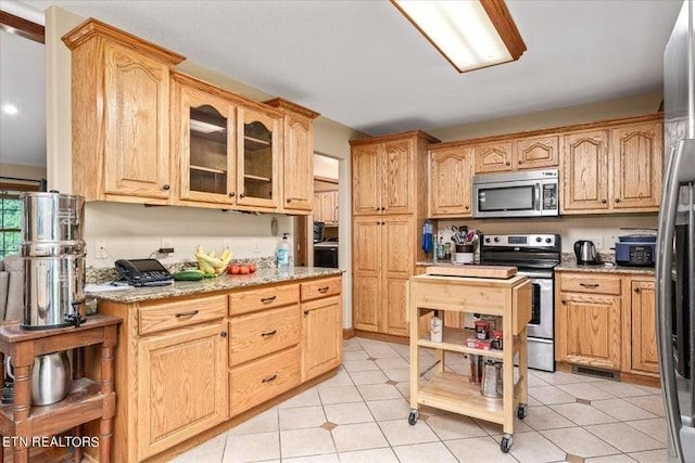 kitchen featuring light stone counters, light brown cabinets, visible vents, appliances with stainless steel finishes, and glass insert cabinets