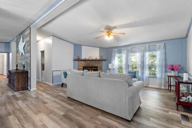 living room featuring ceiling fan, a textured ceiling, a fireplace, and light wood-type flooring