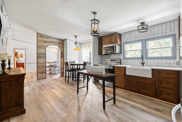 kitchen featuring sink, light hardwood / wood-style flooring, appliances with stainless steel finishes, tasteful backsplash, and decorative light fixtures