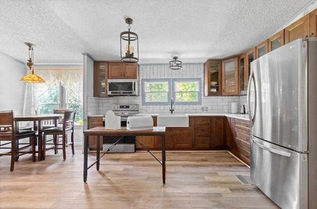 kitchen featuring appliances with stainless steel finishes, pendant lighting, tasteful backsplash, sink, and light hardwood / wood-style flooring