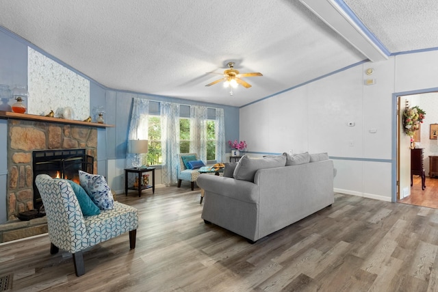 living room featuring a stone fireplace, wood-type flooring, lofted ceiling with beams, a textured ceiling, and ceiling fan