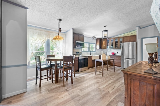 dining space featuring vaulted ceiling, sink, light hardwood / wood-style floors, and a textured ceiling