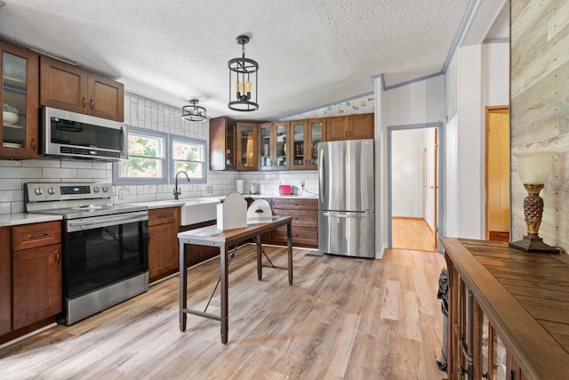 kitchen featuring sink, vaulted ceiling, hanging light fixtures, appliances with stainless steel finishes, and light hardwood / wood-style floors