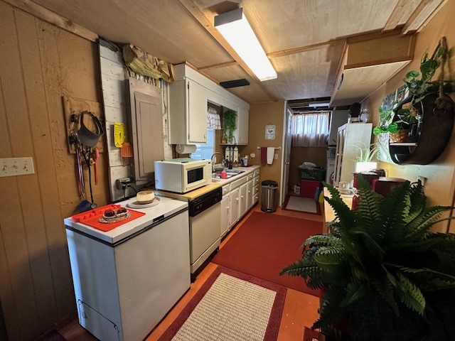 kitchen featuring wood walls, white cabinets, white appliances, and sink