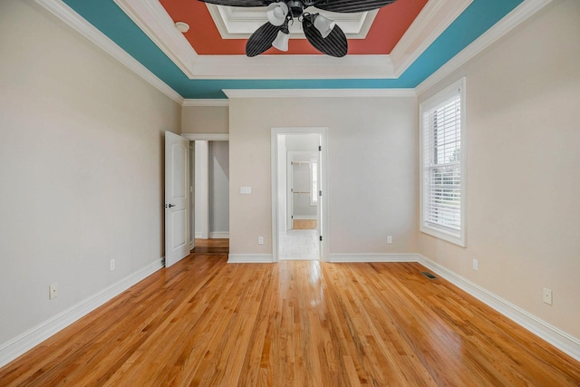 unfurnished bedroom featuring crown molding, ceiling fan, light wood-type flooring, and a tray ceiling