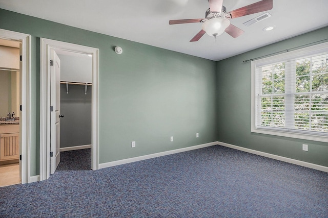 unfurnished bedroom featuring sink, ceiling fan, carpet, a walk in closet, and a closet