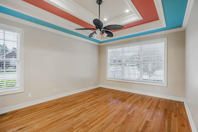 unfurnished room with light wood-type flooring, ornamental molding, ceiling fan, and a tray ceiling