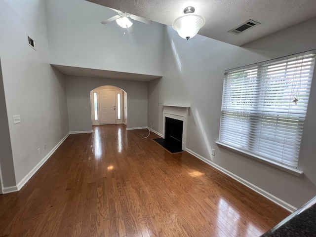 unfurnished living room featuring a towering ceiling, a textured ceiling, wood-type flooring, and ceiling fan