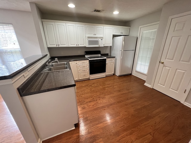 kitchen with kitchen peninsula, dark hardwood / wood-style flooring, white cabinetry, sink, and white appliances