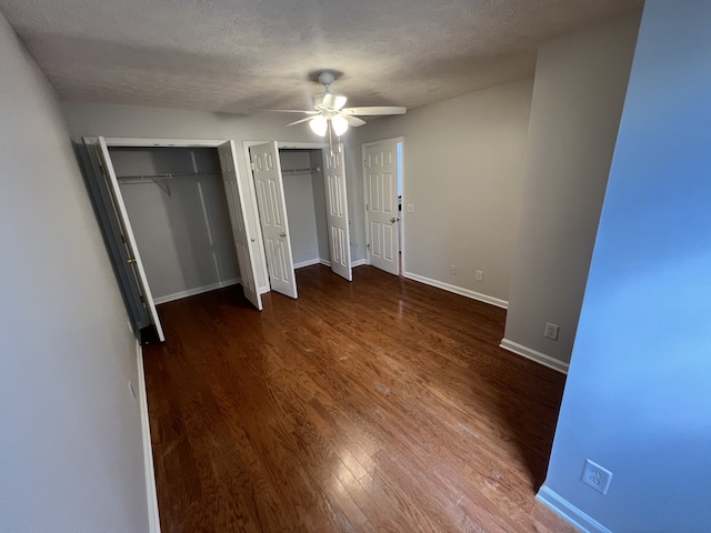 unfurnished bedroom featuring dark wood-type flooring, ceiling fan, multiple closets, and a textured ceiling