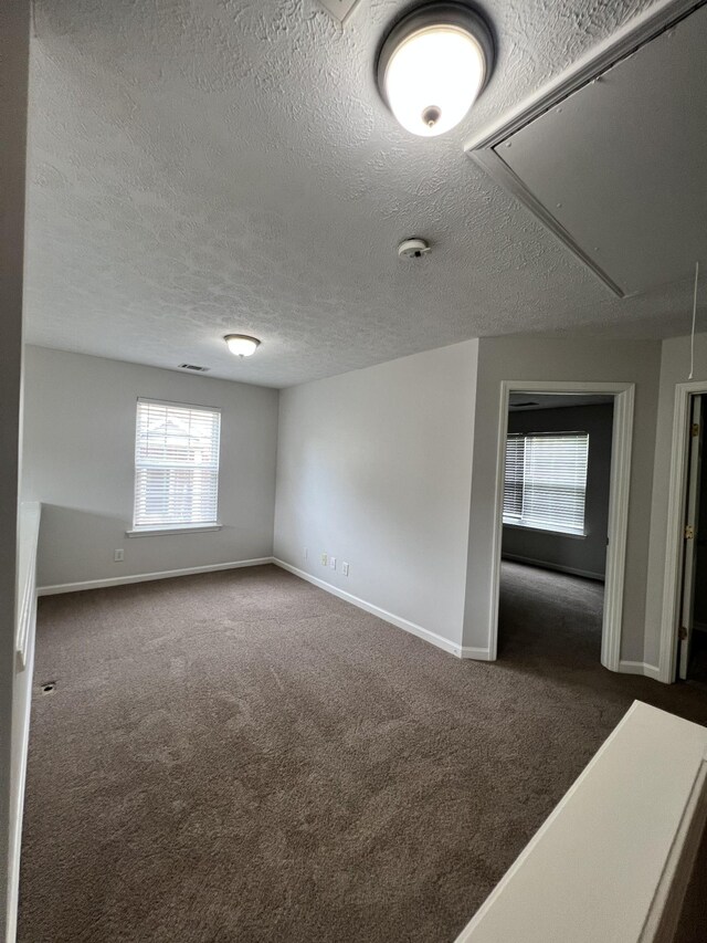 unfurnished room featuring a textured ceiling and dark carpet