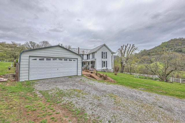 view of front facade featuring a garage, gravel driveway, fence, and a front lawn