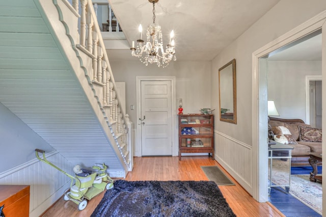 entryway featuring a wainscoted wall, a notable chandelier, visible vents, stairway, and wood finished floors