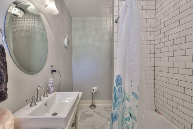 full bathroom featuring marble finish floor, shower / bathtub combination with curtain, baseboards, and a sink