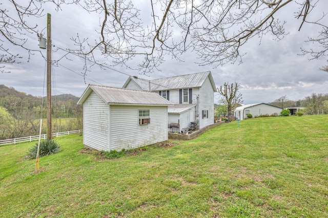 rear view of house with a lawn, metal roof, fence, an outdoor structure, and a shed