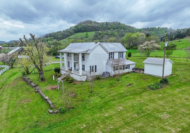 exterior space with a porch, cooling unit, an outdoor structure, a front lawn, and a wooded view