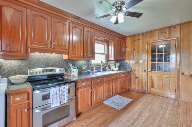 kitchen with range with two ovens, light wood-style floors, brown cabinetry, and a sink