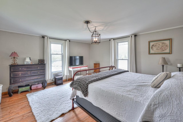 bedroom featuring a chandelier, crown molding, baseboards, and wood finished floors