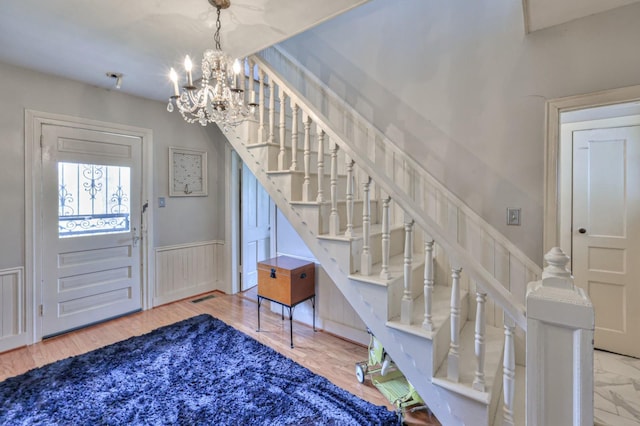 foyer entrance with stairs, a chandelier, a decorative wall, and wainscoting