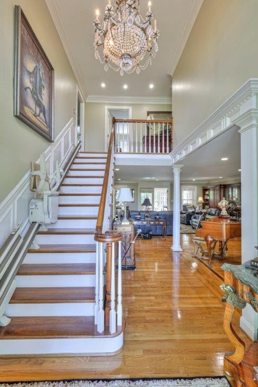 entrance foyer featuring light hardwood / wood-style flooring, ornamental molding, decorative columns, and a notable chandelier