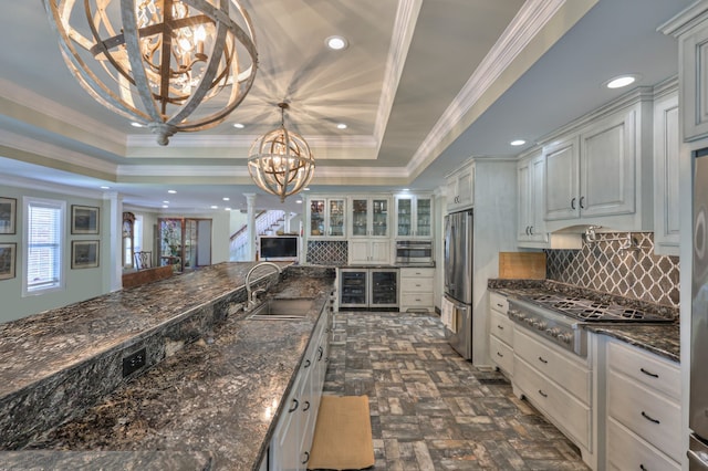 kitchen featuring a raised ceiling, crown molding, an inviting chandelier, stainless steel appliances, and sink