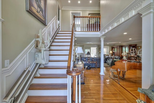 staircase featuring decorative columns, wood-type flooring, and ornamental molding