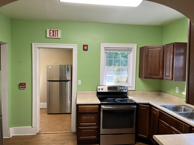 kitchen featuring appliances with stainless steel finishes, light hardwood / wood-style flooring, dark brown cabinets, and sink