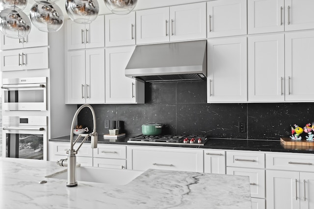 kitchen featuring white cabinetry, wall chimney range hood, backsplash, stainless steel appliances, and sink