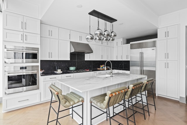 kitchen featuring appliances with stainless steel finishes, backsplash, light parquet floors, sink, and wall chimney exhaust hood