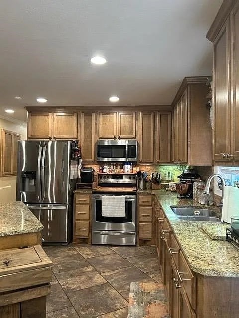 kitchen with appliances with stainless steel finishes, sink, dark tile patterned floors, and light stone counters