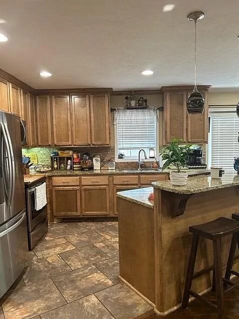 kitchen featuring decorative backsplash, light stone counters, appliances with stainless steel finishes, a kitchen breakfast bar, and sink