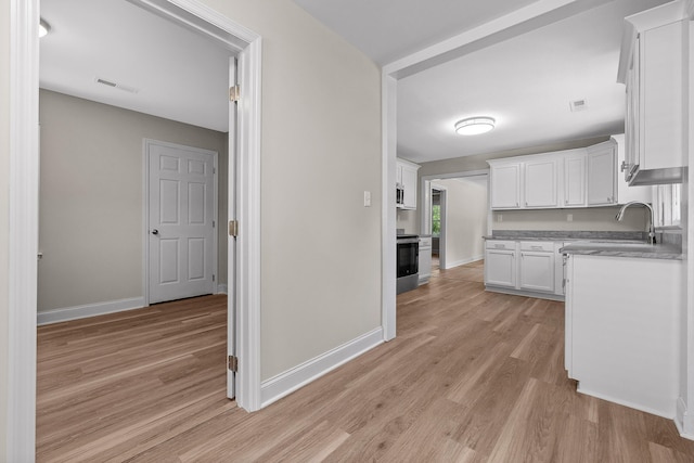 kitchen with range, white cabinets, sink, and light hardwood / wood-style floors