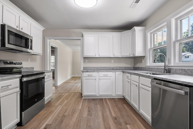 kitchen with light hardwood / wood-style floors, dishwashing machine, white cabinets, sink, and stove