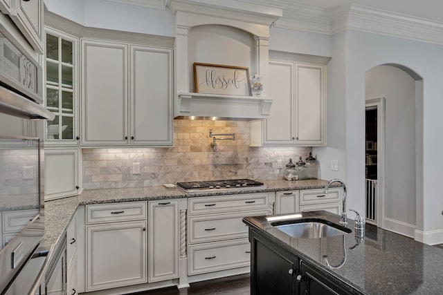 kitchen featuring custom exhaust hood, sink, backsplash, dark stone counters, and stainless steel gas cooktop