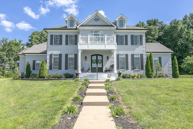 view of front facade with a balcony, french doors, and a front lawn