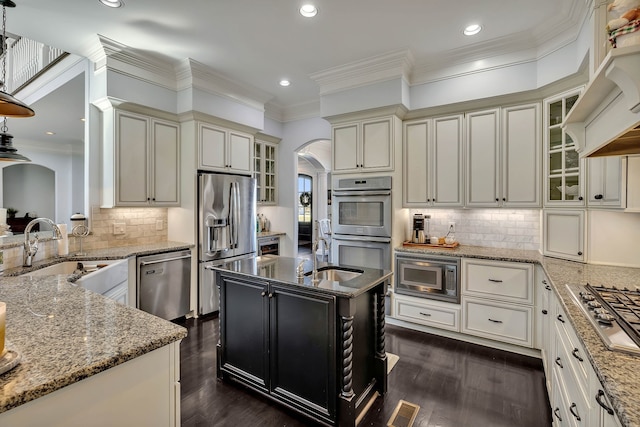 kitchen featuring appliances with stainless steel finishes, a kitchen island with sink, dark wood-type flooring, light stone countertops, and tasteful backsplash