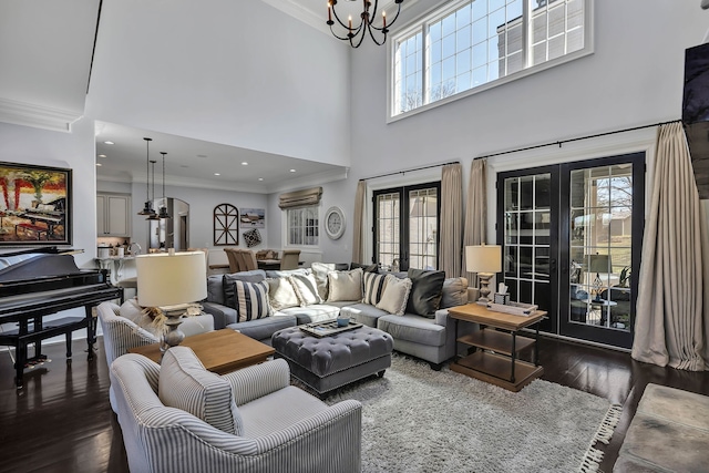 living room featuring dark hardwood / wood-style flooring, a notable chandelier, french doors, ornamental molding, and a towering ceiling