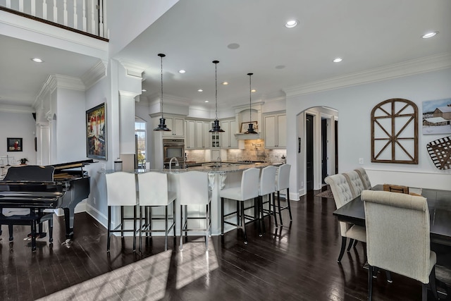 kitchen with light stone counters, ornamental molding, tasteful backsplash, dark hardwood / wood-style flooring, and a breakfast bar area