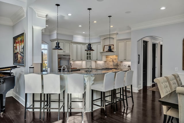 kitchen with tasteful backsplash, appliances with stainless steel finishes, dark wood-type flooring, premium range hood, and a breakfast bar area