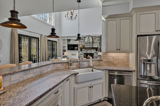 kitchen with a fireplace, stainless steel appliances, light stone countertops, backsplash, and sink