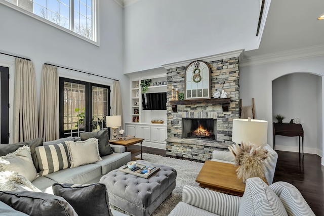 living room featuring built in features, a stone fireplace, wood-type flooring, and a wealth of natural light