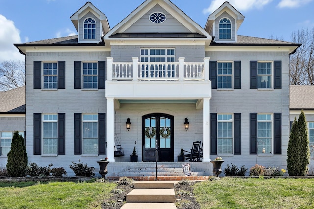 view of front of house with a balcony, french doors, and a front lawn