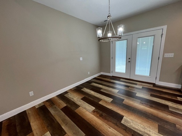 unfurnished dining area with french doors, dark hardwood / wood-style floors, and an inviting chandelier