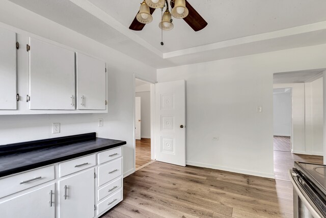 kitchen with light hardwood / wood-style flooring, ceiling fan, white cabinets, range, and a tray ceiling