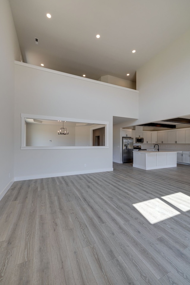 unfurnished living room with light wood-type flooring, sink, and a high ceiling