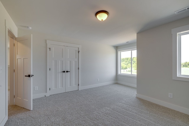 unfurnished bedroom with light carpet, a closet, and multiple windows